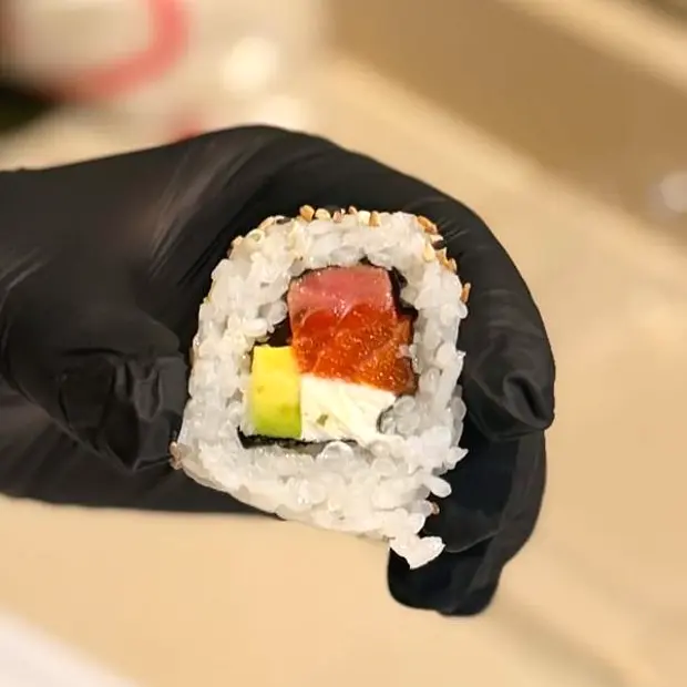 Roll de Nami recién cortado, en la mano: salmón, atún, palta y queso.